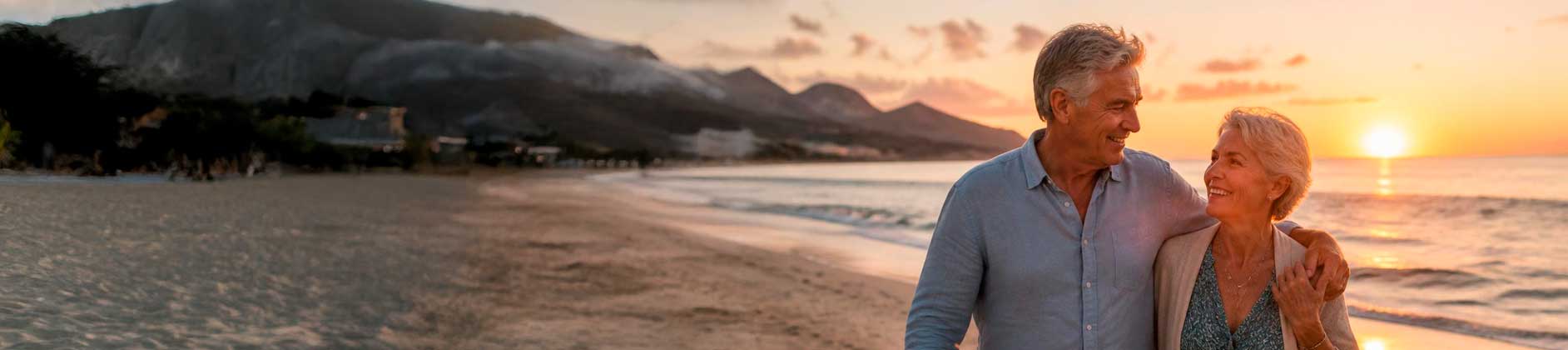Casal acima de 60 anos caminhando feliz na praia ao pôr do sol